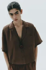 Camisa marrón de cuello solapa y escote pico con manga corta. Bolsillos de plastrón en pecho. Cierre frontal con botones.