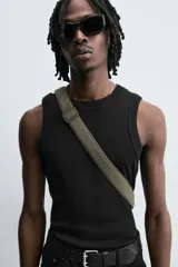 Bandolera negra de tela técnica con correa ajustable. Tiene un compartimento principal con cierre de solapa e imán, y un bolsillo plano interior.