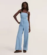 Mono largo de jeans celeste con breteles finos ajustables, escote cuadrado, recortes delanteros y laterales abiertos, lazo en la espalda y elástico en la cintura.