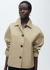 Chaqueta color beige de corte recto con cuello camisero, cierre frontal con botones y mangas largas.
