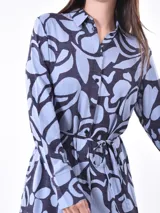 Vestido midi camisero con estampado abstracto en tonos celeste y azul marino. Tiene cuello camisero, mangas largas y lazo en la cintura.