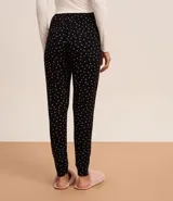 Pantalón de pijama jogger negro con estampado de lunares blancos y lazo rosa en la cintura.