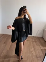 Conjunto negro brillante compuesto por un top corto con escote off-shoulder y mangas anchas, y una falda corta con lazo lateral.