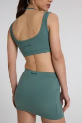 Top deportivo verde con doble escote superpuesto, confeccionado en textil Activelu con compresión media, protección UV50+ y nula transparencia.