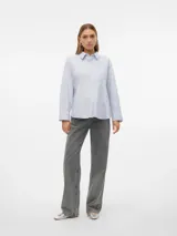 Camisa celeste de corte oversize, con cuello clásico, cierre frontal con botones, bolsillo en el pecho y mangas largas con puños abotonados.