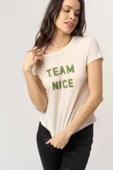 Remera de manga corta color crema o blanco roto, confeccionada en tejido jersey liviano y suave, con cuello redondo. Presenta el texto "TEAM NICE" estampado en dos líneas, con letras verdes y contorno rojo.