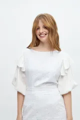 Blusa blanca con mangas abullonadas y volados en las sisas. El cuerpo de la blusa es de tela bordada con pequeños orificios.