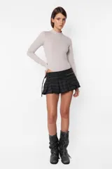 Minifalda gris con estampado de cuadros escoceses, cintura ancha, tablas en la parte inferior y cierre metálico lateral. Incluye sobrefalda desmontable con bolsillo.