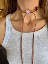 Gargantilla de cuero marrón con flores de acrílico rosado y tiras de cuero para atar.