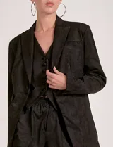 Blazer negro de gamuza con cuello solapado, cierre frontal con un solo botón forrado y bolsillos de parche en la parte delantera. Presenta un tajo vertical en la espalda.