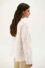 Camisa blanca con bordado floral, de corte holgado y manga larga.