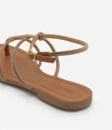 Sandalias planas tipo gladiadoras color tostado, con tiras finas con strass, punta redonda y cierre con hebilla en el tobillo.