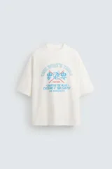 Remera color hueso de corte holgado con estampado celeste y azul con texto y dibujo de un castor con banderas a cuadros.