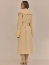 Abrigo trench maxi color beige con ribete de piel sintética en cuello y puños.
