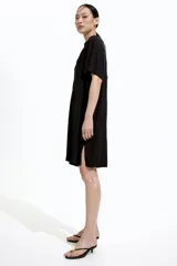 Vestido túnica negro a la rodilla en tejido liviano de viscosa con cuello mao y abertura en V. Modelo de corte holgado con hombros levemente caídos, mangas cortas y bajo recto con tajos laterales.
