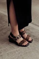 Sandalia de cuero color negro con taco bloque medio y punta cuadrada. Presenta dos tiras anchas sobre el empeine, una de ellas con hebilla metálica dorada, y una tira de sujeción en el talón. Posee base acolchonada para mayor comodidad.