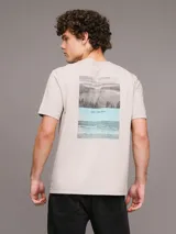 Remera color beige de algodón regenerativo con cuello redondo, mangas cortas y logo CK bordado en el pecho. Presenta un diseño de paisaje gráfico en el frente.