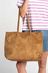 Bolso tipo tote de gamuza vegana color camel, con asas de mano y logo grabado en el frente.