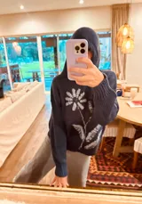 Hoodie azul marino de tejido de lana con bordado de una flor blanca en el frente.