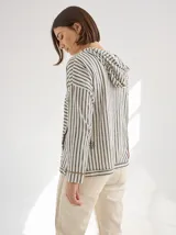 Chomba a rayas horizontales color crudo y gris, con capucha y botones de madera. Tiene cordones de ajuste en la capucha y puños con ribete verde flúor.