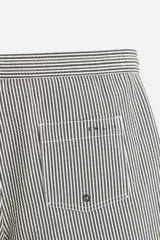 Short de baño con textura seersucker a rayas verticales azul marino y blanco. Tiene cintura elástica ajustable con cordón, bolsillos frontales y traseros, aberturas laterales en el bajo y forro interior.