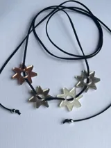 Gargantilla con cordón negro ajustable y dijes de estrellas caladas en tonos plateado, dorado y cobre.
