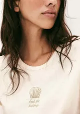 Pijama de dos piezas compuesto por una remera de manga corta color crema con un pequeño bordado de concha marina y un short de tiro alto con elástico y estampado de cuadrícula en tonos beige y blanco.