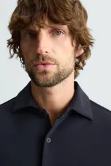 Camisa color beige de corte slim fit, confeccionada en tejido elástico que minimiza las arrugas. Tiene cuello italiano abierto, manga larga con puños abotonados y cierre frontal con botones.