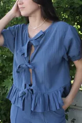 Camisa azul de tusor 100% algodón, con escote en V y mangas cortas abullonadas. Presenta volados en el ruedo y cierre frontal con lazos.