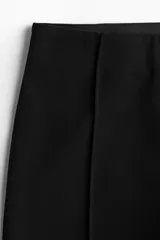 Pantalón negro de sarga con tiro alto, elástico oculto en la cintura y cierre lateral oculto. Piernas ajustadas con bajo levemente acampanado.