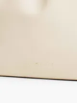 Cartera bombonera color crema con asa corta y correa larga extraíble. Tiene cierre con cordón ajustable y detalles metálicos dorados.