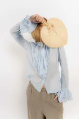 Camisa celeste de algodón con cuello alto y volados frontales. Mangas largas con puños fruncidos.