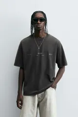 Camiseta negra de corte relaxed fit, cuello redondo y manga corta. Tiene un texto en relieve combinado a contraste en el delantero y efecto lavado.