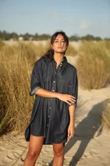 Vestido camisero corto de jean azul oscuro, con cuello clásico, mangas 3/4 con puños arremangados y cierre frontal con botones dorados.