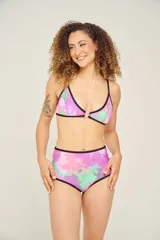 Conjunto de bikini estampado con flores y hojas en tonos celeste, turquesa, rosa y violeta. El corpiño es deportivo con breteles negros y la bombacha es de tiro alto con ribete negro.