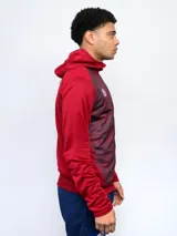 Campera de entrenamiento con capucha, cierre frontal y puños y cintura de tela acanalada. El cuerpo de la campera es azul con un estampado moteado en tonos de azul más claro, mientras que las mangas y la capucha son de color azul liso. Lleva el escudo del Club Nacional de Football y el logo de Umbro bordados en el pecho.