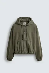 Cazadora verde militar con capucha ajustable, cierre frontal con cremallera, bolsillos tipo canguro y mangas largas con puños elásticos. Tiene un corte relaxed fit y efecto lavado.