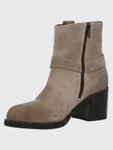 Bota corta de cuero color taupe, con caña de 14 cm, taco cuadrado de 6 cm y punta cuadrada. Presenta una correa con hebilla metálica alrededor del tobillo y cierre lateral.