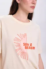 Remera color crema de corte recto, con mangas cortas y estampa de medio sol con el texto "Sun & Beach" en color naranja.