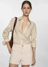 Short color crema de tiro alto, con bolsillos de parche delanteros y traseros, cierre frontal con cremallera y botón, y trabillas para cinturón.