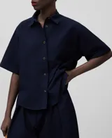 Camisa azul marino de algodón seersucker con cuello solapa, manga corta sobre el codo, botonadura frontal y aberturas frontales en el bajo.