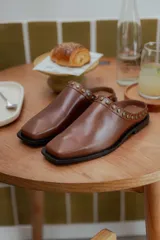 Mules de cuero negro con punta cuadrada y detalle de tachas plateadas en el borde superior.