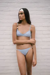 Conjunto de bikini celeste con corpiño triangular con breteles regulables y espalda para atar. Detalle de abalorios en los breteles. Incluye copas desmontables. La bombacha es semivedetina regulable con detalle de abalorios en uno de los breteles laterales.