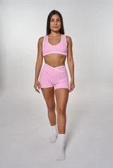 Conjunto deportivo rosa con top y short. El top es tipo corpiño con breteles y el logo 'bk.' estampado. El short es de tiro alto con cintura cruzada.