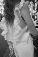 Blusa blanca semitransparente de cuello redondo y sin mangas, con volantes en los hombros y en el frente.