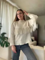 Sweater de lana color crema, con cuello redondo y mangas largas. Presenta una banda horizontal de flecos en el pecho.