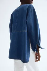 Blusa azul de denim con cuello redondo, tapeta con botones ocultos y mangas largas con puños abotonados.