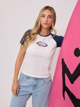 Remera blanca con mangas raglán azul marino y estampado ovalado con el logo de Rusty en el pecho.