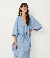 Kimono de lyocell (tejido tipo jean) color celeste claro con estampado repetitivo de pequeños peces blancos. Diseño de manga corta ancha y abertura frontal que se ajusta con un lazo fino en la cintura.