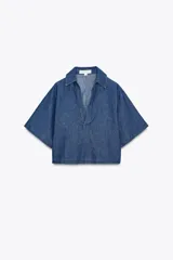 Camisa corta de denim azul, con cuello solapa, escote en pico y mangas cortas.